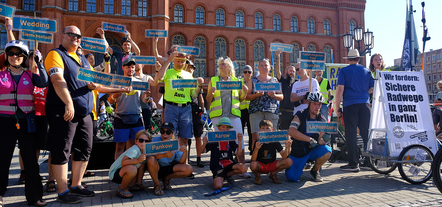 Demo Radschnellwegestopp 8.9.2024 Menschen halten vor dem Roten Rathaus diverse Berliner Ortsteilschilder in die Höhe