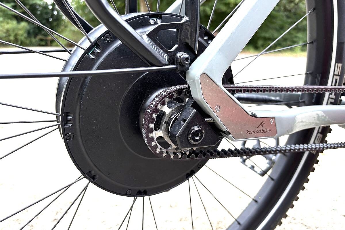 Großaufnahme eines schwarzen Hinterradmotors, davor der Antriebsrimen, an einem grauen Fahrrad. 